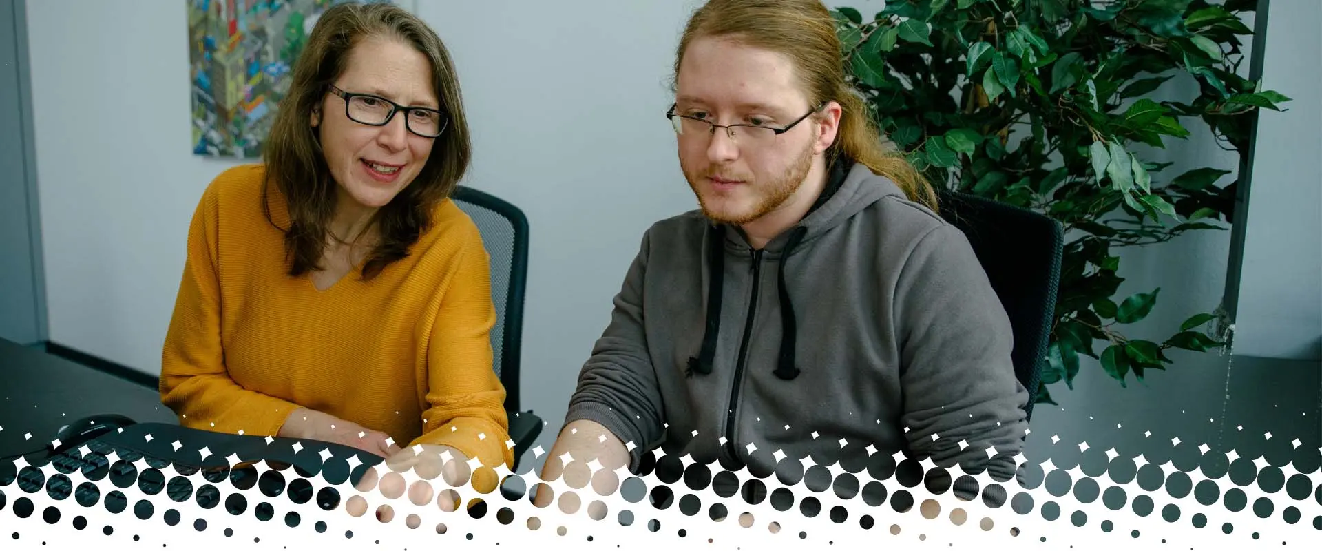 Zwei Kolleginnen und Kollegen arbeiten konzentriert gemeinsam an einem Computer in einem modernen Büro.