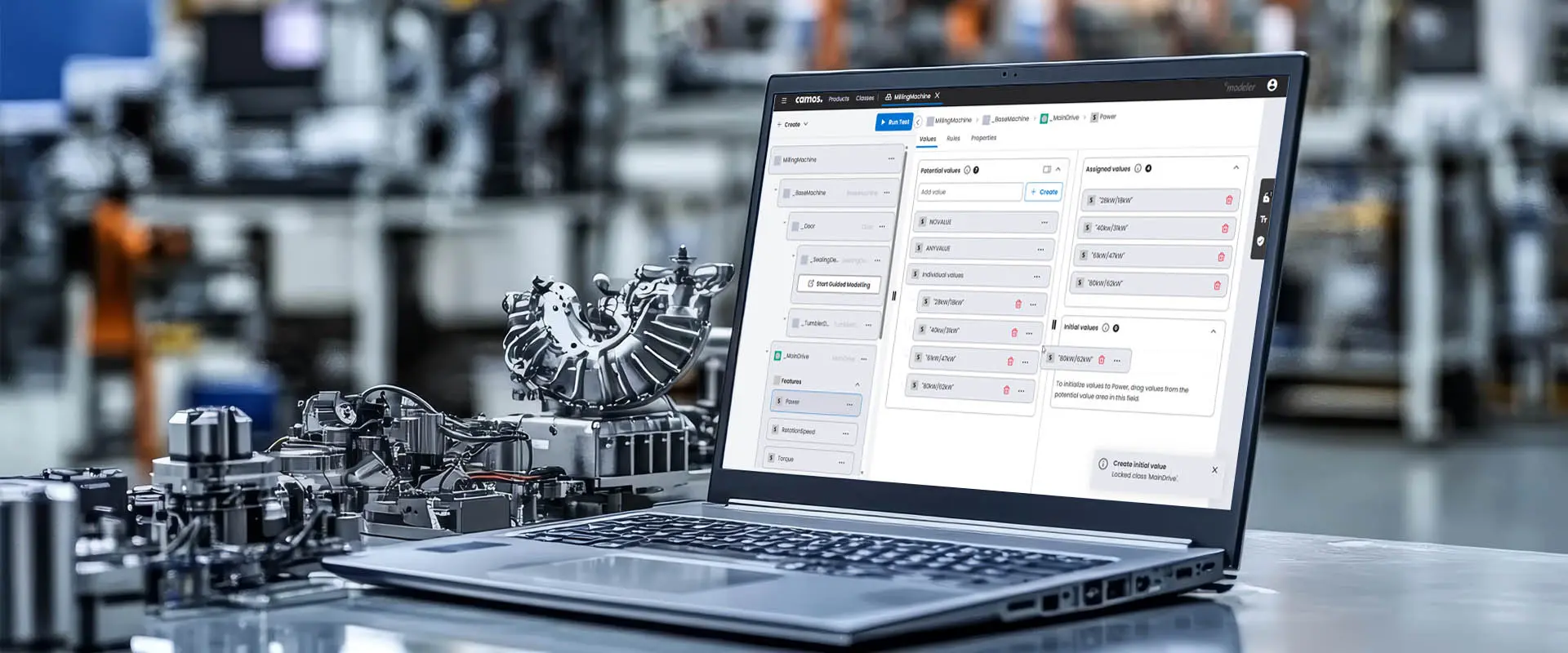 Offenes Laptop mit geöffnetem Modellierungs-Tool auf einem Tisch in einer modernen Industrieumgebung. Im Hintergrund sind unscharf Maschinen und Fertigungsteile zu sehen, im Vordergrund liegt ein komplexes Maschinenteil neben dem Laptop.