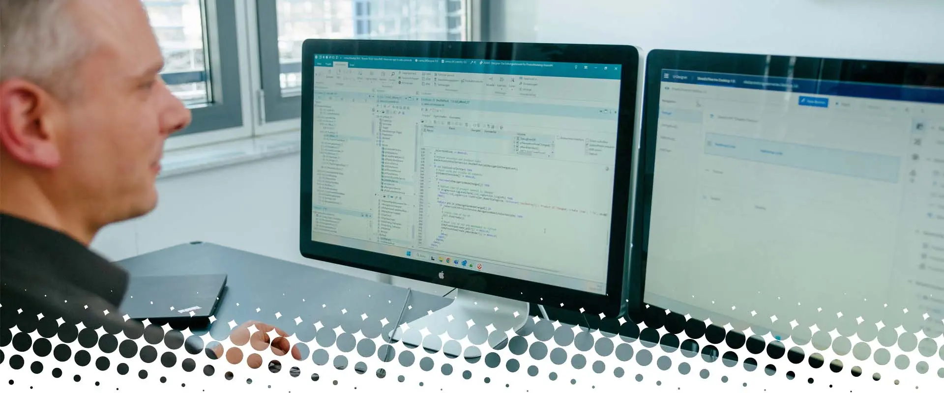 An employee working on two screens with the camos CPQ software in a modern office.